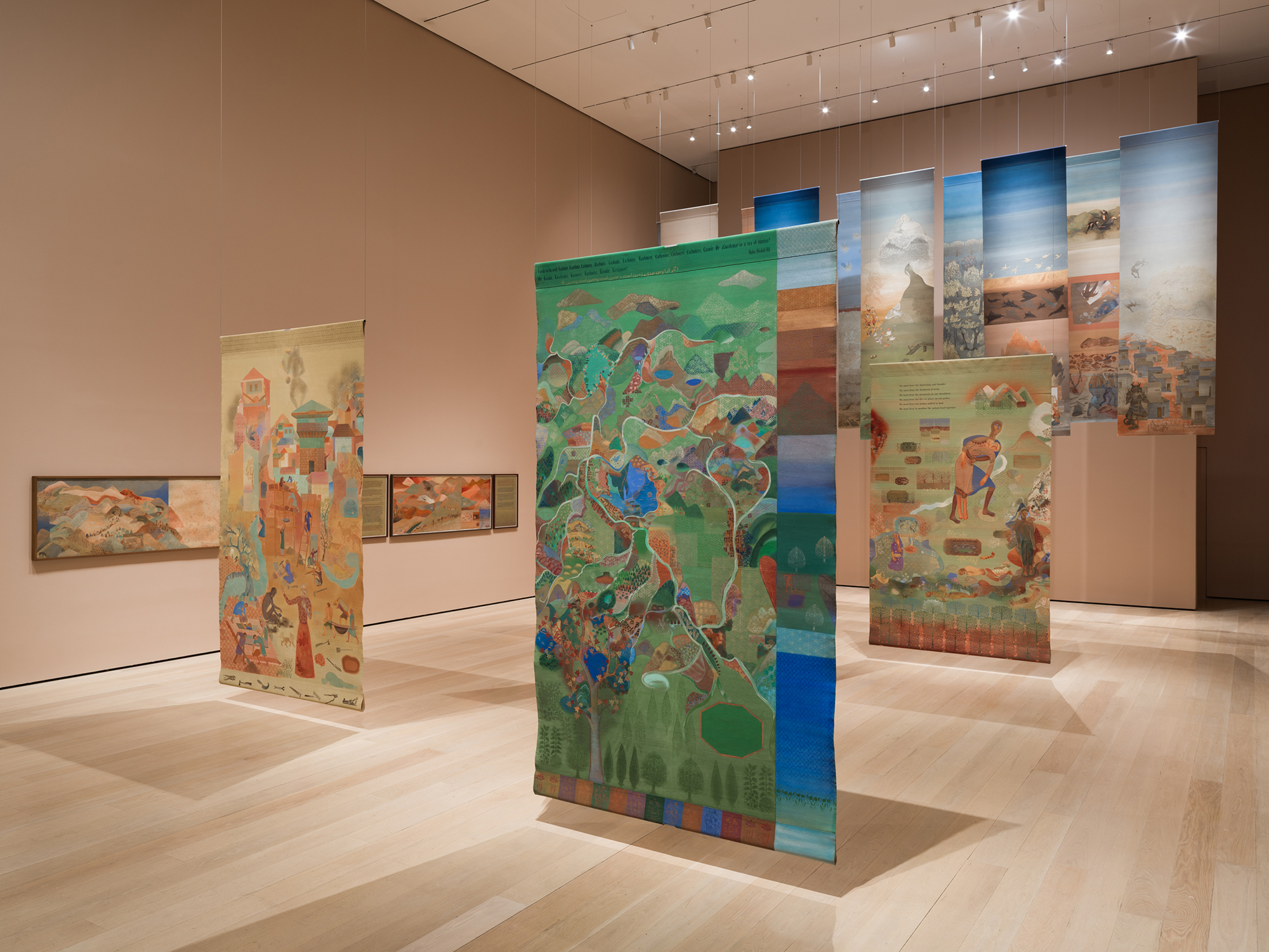 Colorful painted scrolls depicting landscapes and figures hang from the ceiling in Nilima Sheikh’s Fractured Skies exhibition at MoMA.